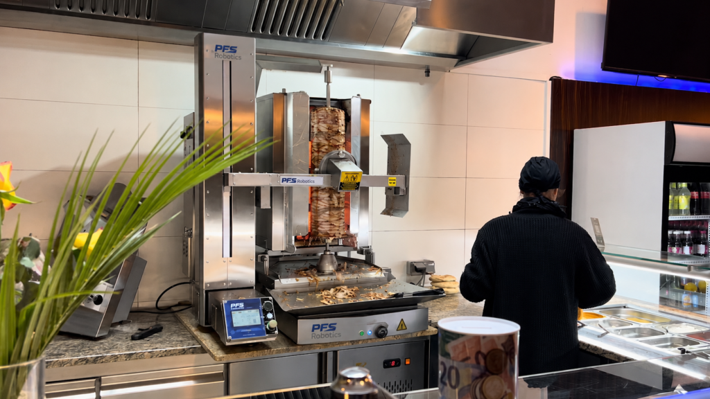 Restoran ortamında döner kesen fast food modeli robot ve arkası dönük şekilde dürüm hazırlayan kadın çalışan